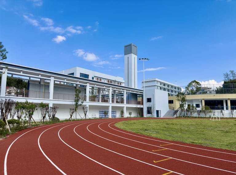 A modern sports facility with a red running track and towers on a sunny day.