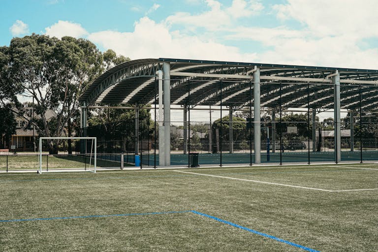 A versatile sports facility featuring a roofed court and soccer field under a bright sky.