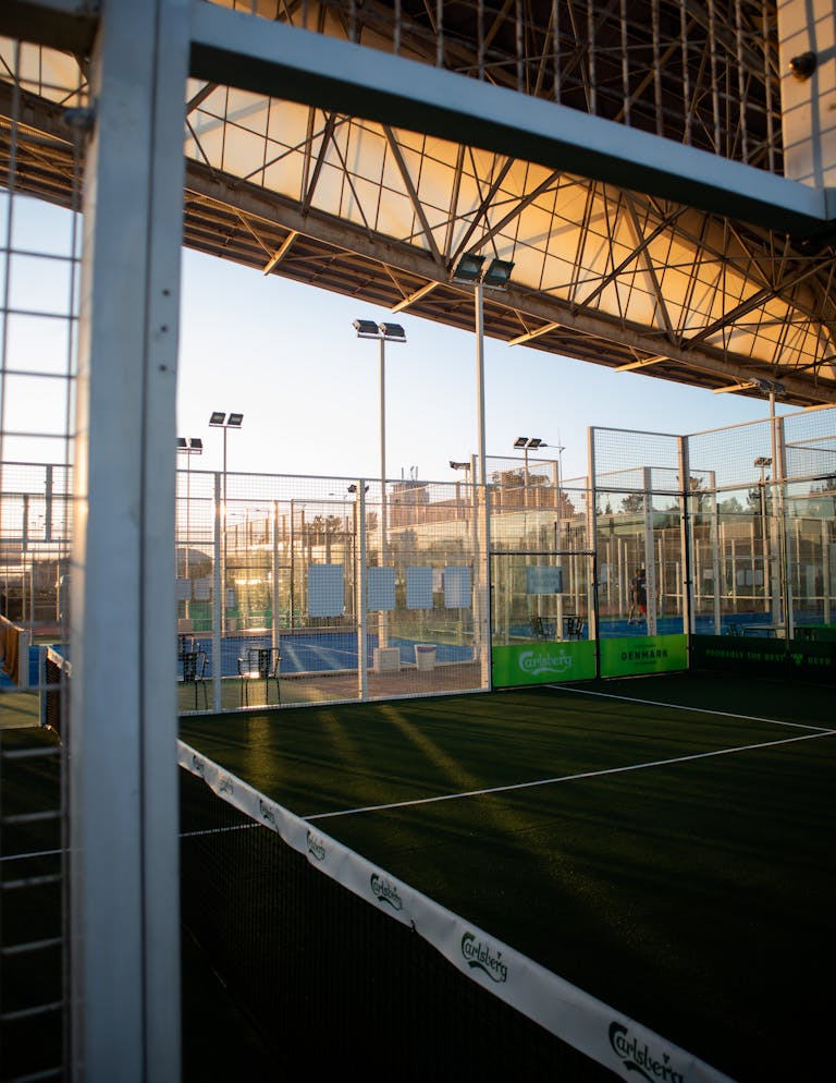 Indoor tennis court with net setup, lighting, and architectural design under a glass roof.